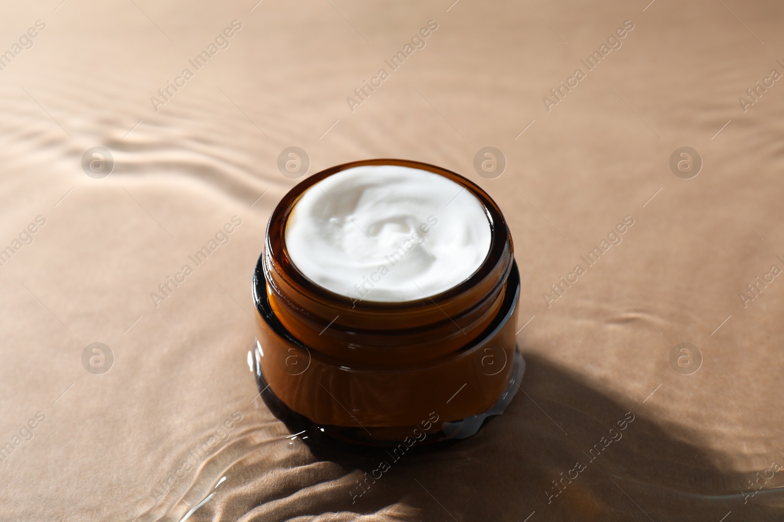 Photo of Jar with face cream in water on beige background