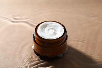 Photo of Jar with face cream in water on beige background