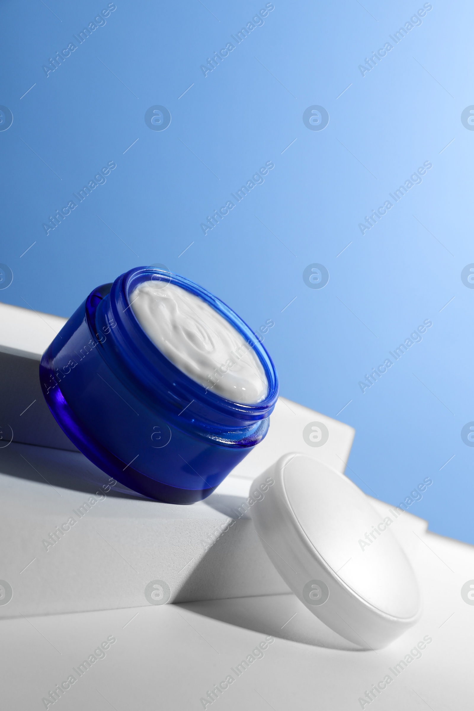 Photo of Stylish presentation of face cream in jar against light blue background