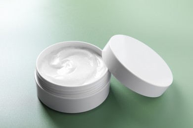 Face cream in jar on green background, closeup