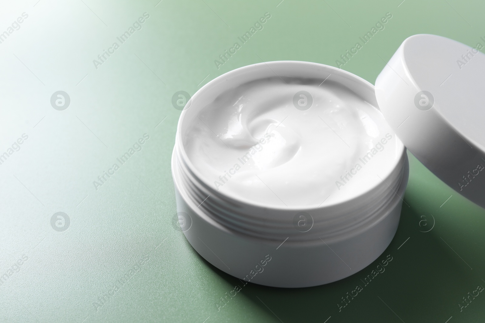 Photo of Face cream in jar on green background, closeup. Space for text