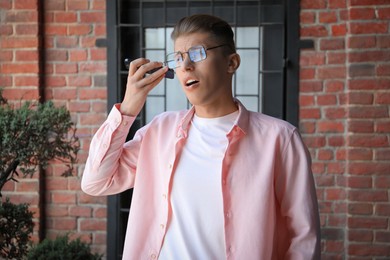 Photo of Young man with smartphone listening to voice message outdoors