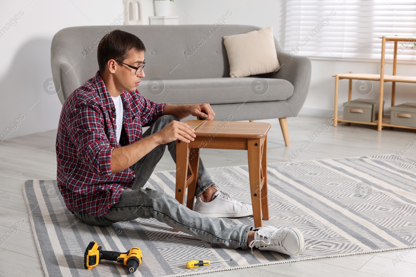 Photo of Man using tape measure while repairing wooden stool indoors