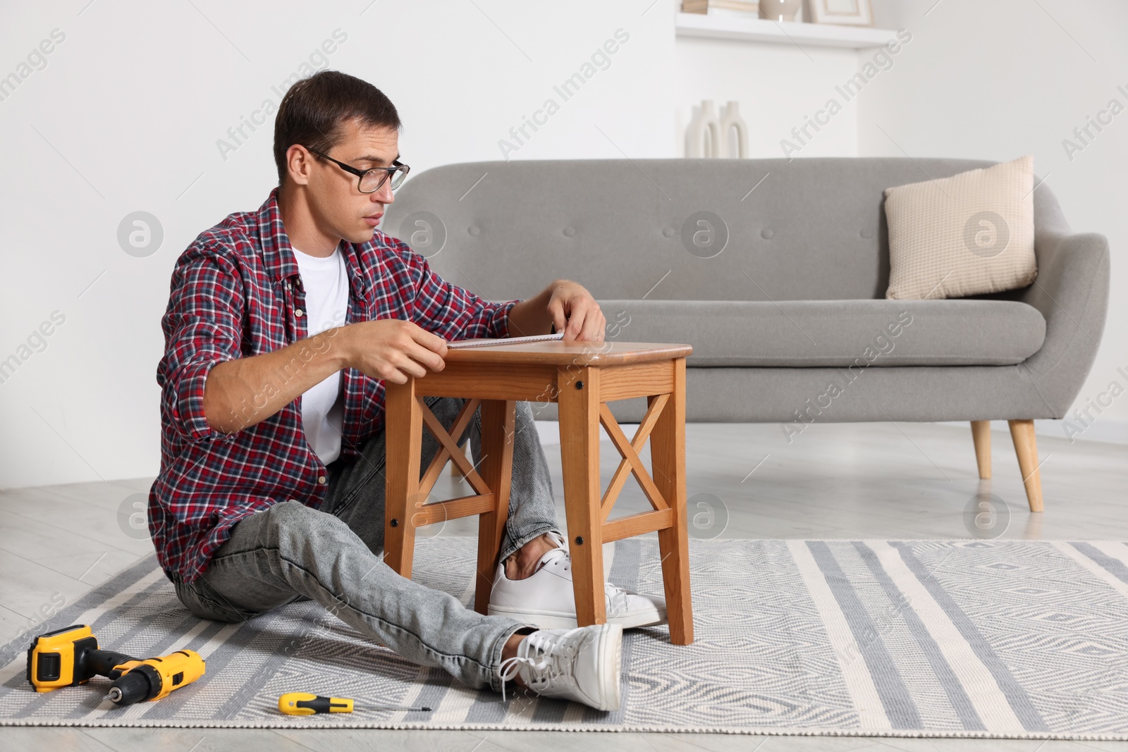 Photo of Man using tape measure while repairing wooden stool indoors