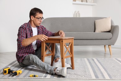 Man using tape measure while repairing wooden stool indoors