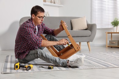 Man repairing wooden stool with screwdriver indoors