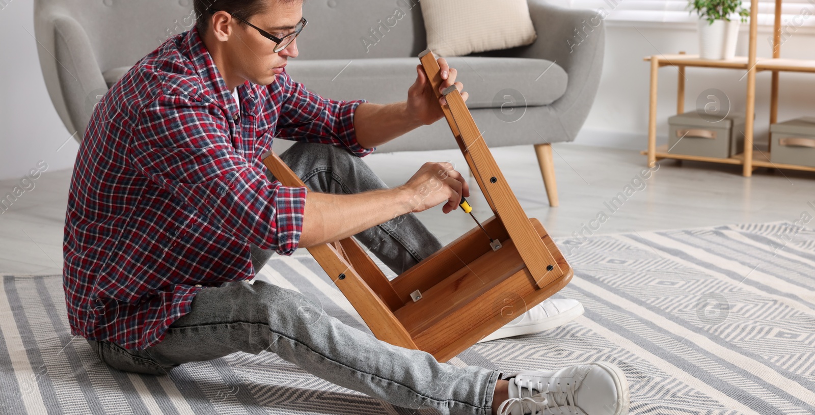 Photo of Man repairing wooden stool with screwdriver indoors