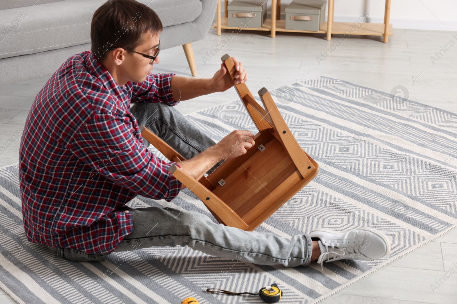 Photo of Man repairing wooden stool with screwdriver indoors