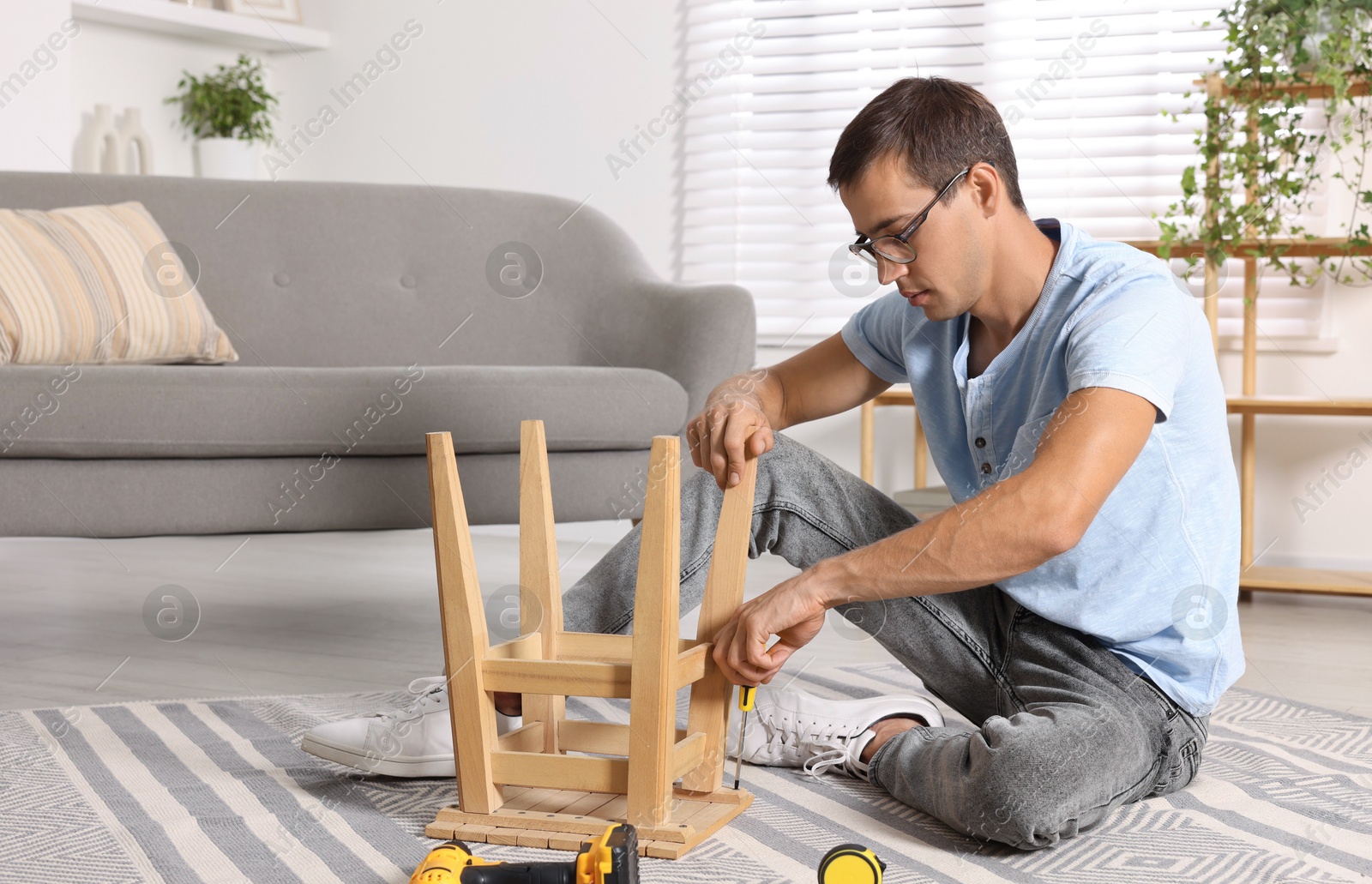 Photo of Man repairing wooden stool with screwdriver indoors