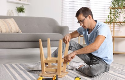 Photo of Man repairing wooden stool with screwdriver indoors