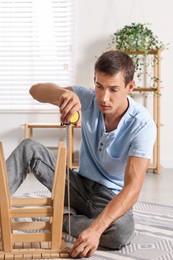 Man using tape measure while repairing wooden stool indoors