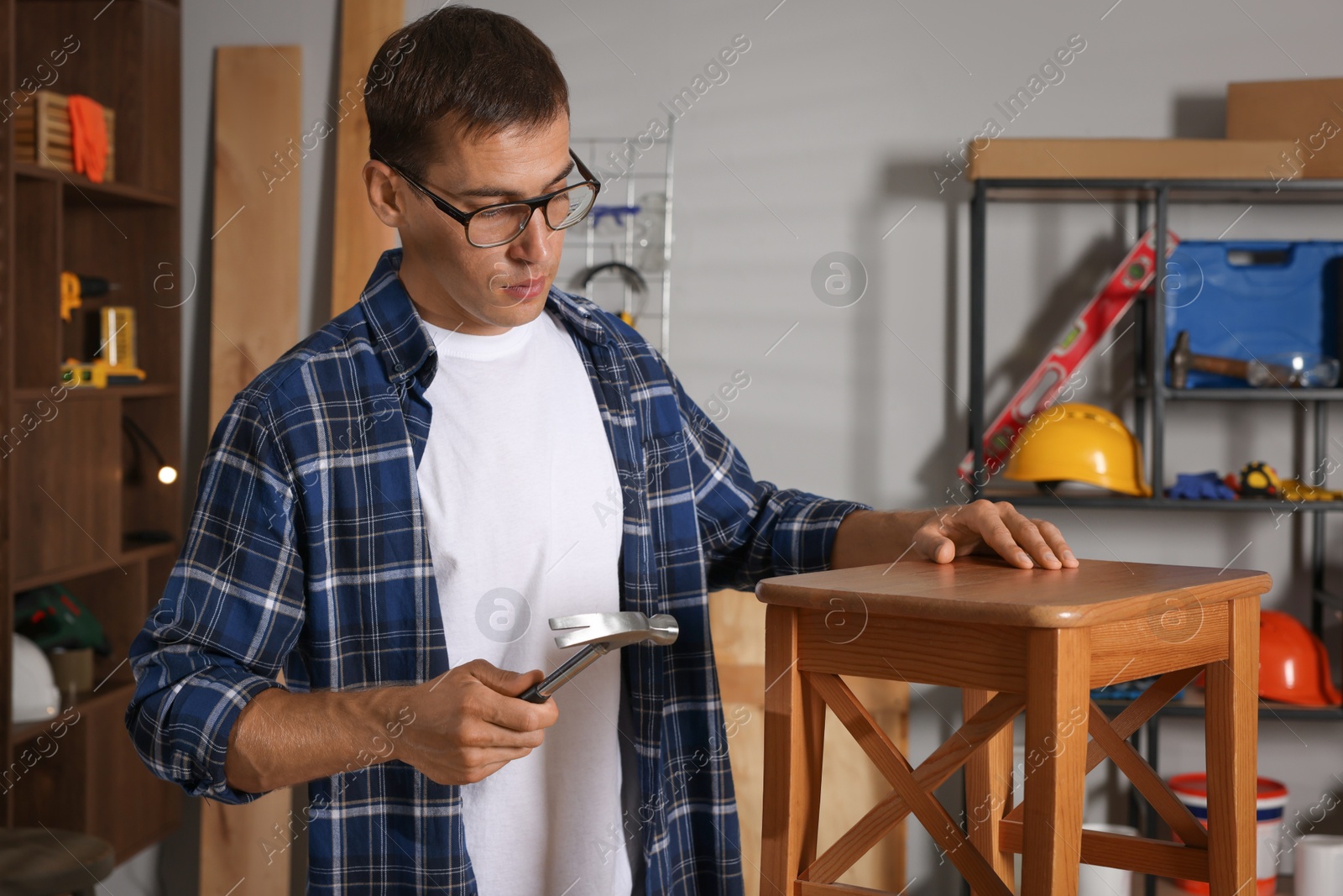 Photo of Man repairing wooden stool with hammer indoors