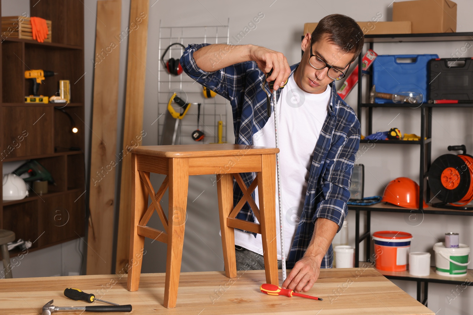 Photo of Man using tape measure while repairing wooden stool indoors