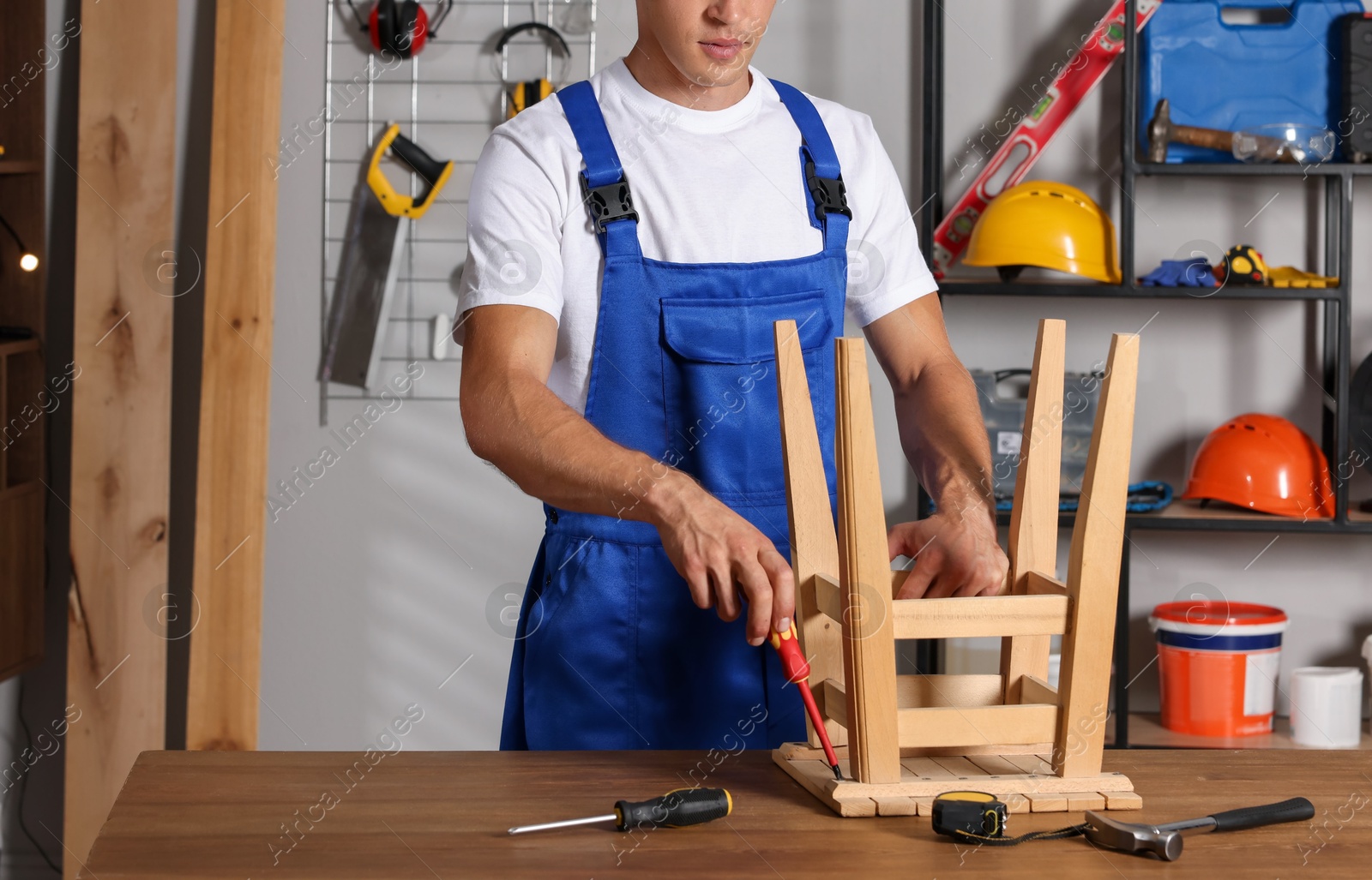 Photo of Man repairing wooden stool with screwdriver indoors, closeup