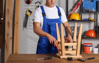 Man repairing wooden stool with screwdriver indoors, closeup