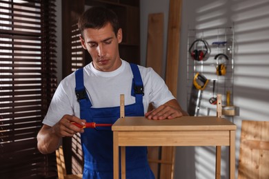 Man repairing wooden stool with screwdriver indoors