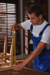 Photo of Man using tape measure while repairing wooden stool indoors