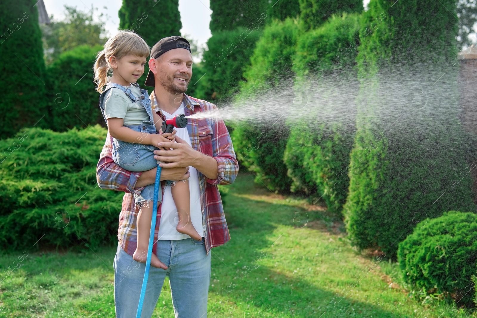 Photo of Father and his daughter watering lawn with hose in backyard