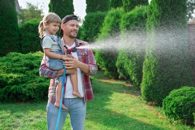 Father and his daughter watering lawn with hose in backyard