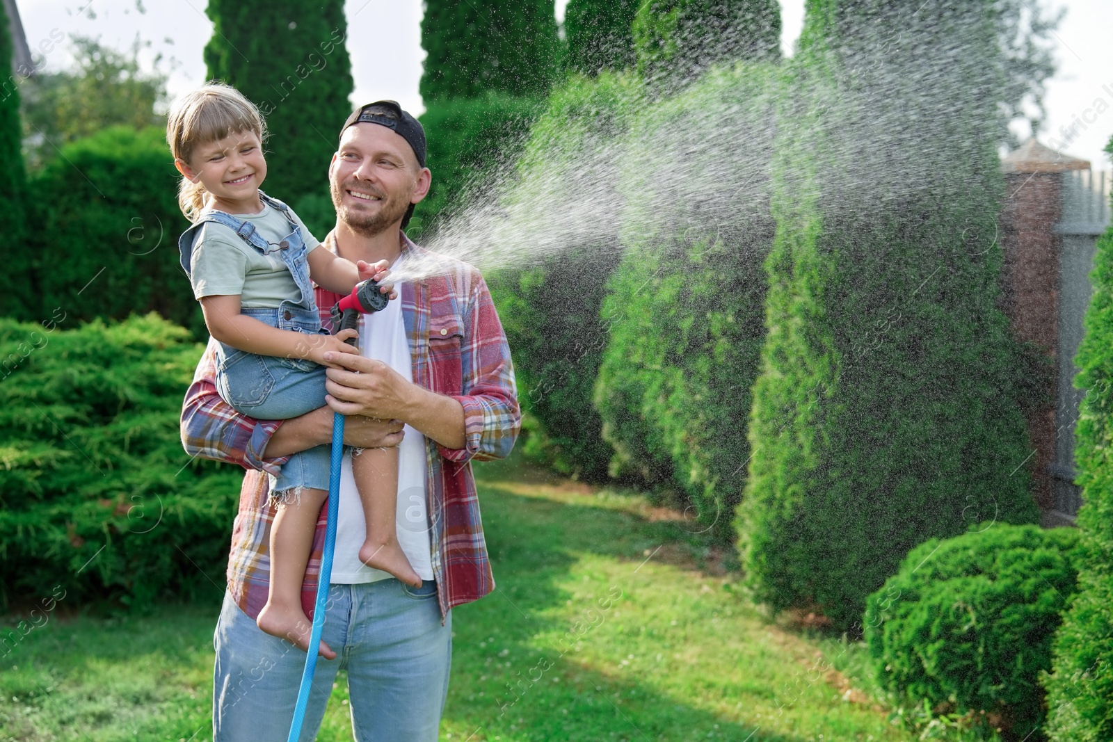 Photo of Father and his daughter watering lawn with hose in backyard