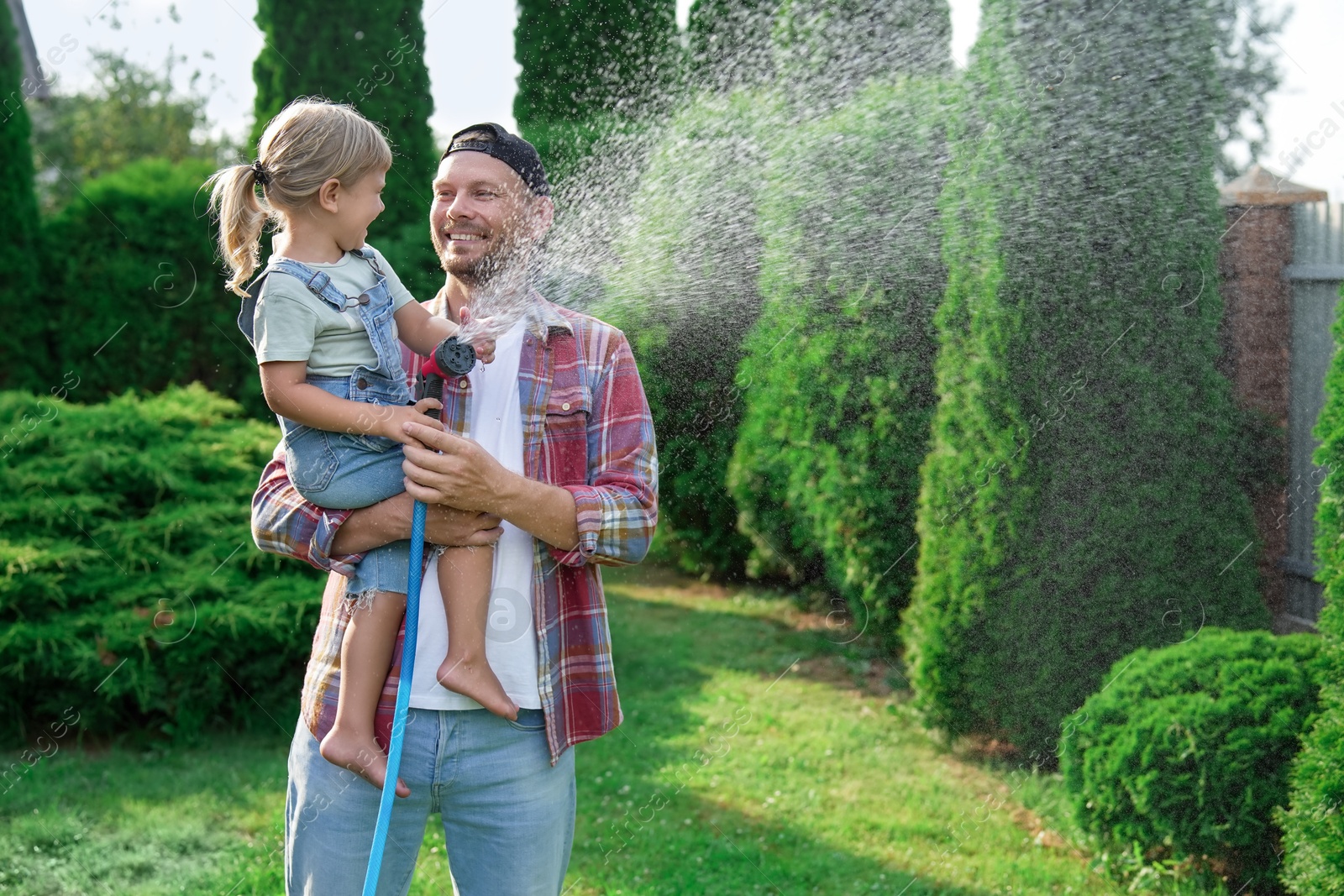 Photo of Father and his daughter watering lawn with hose in backyard