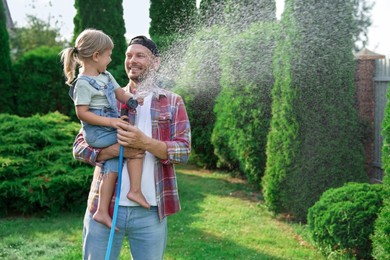 Photo of Father and his daughter watering lawn with hose in backyard