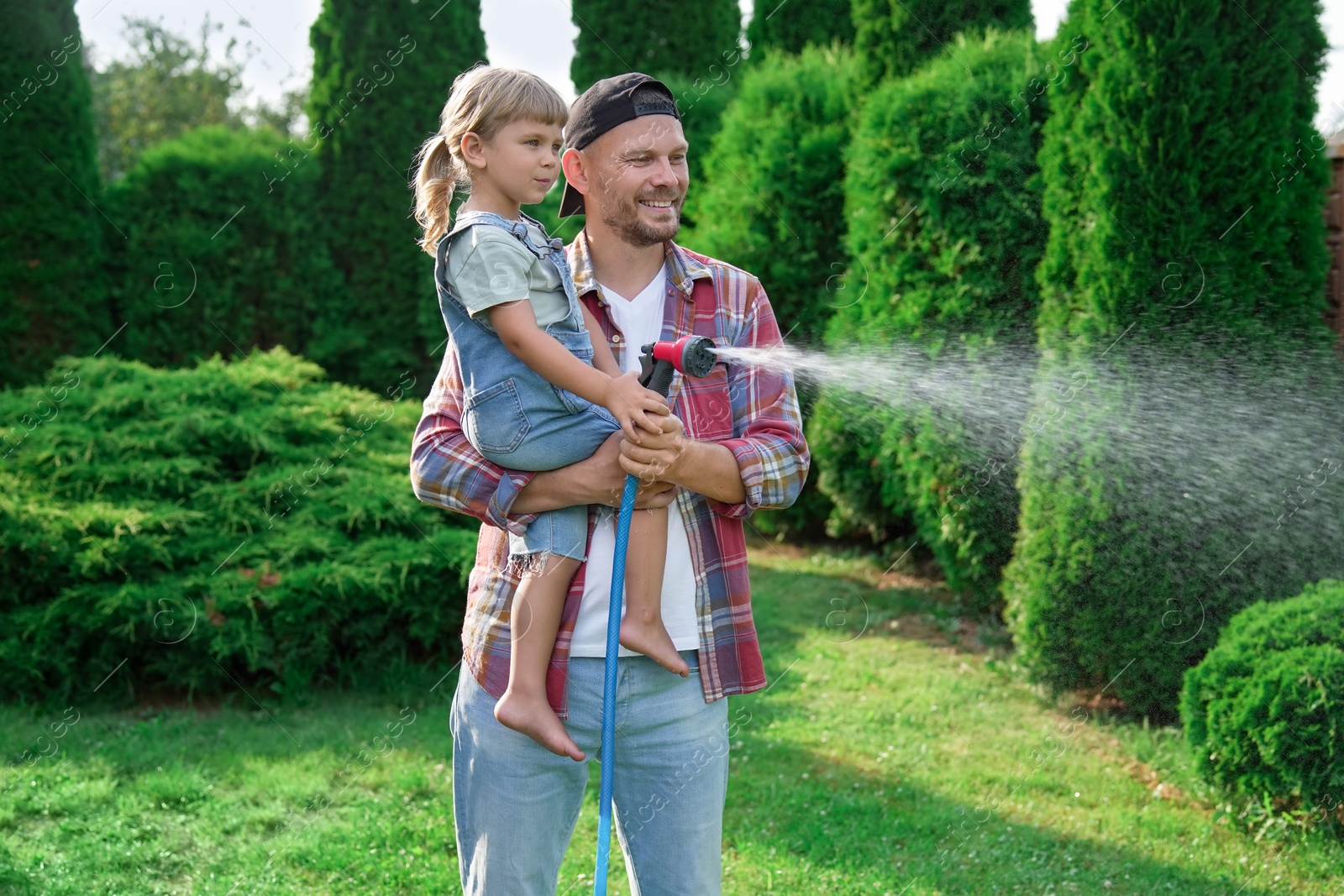 Photo of Father and his daughter watering lawn with hose in backyard