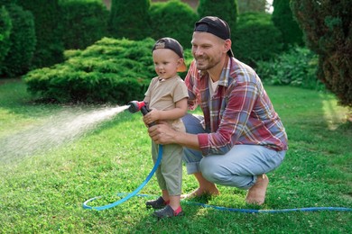 Father and his son watering lawn with hose in backyard