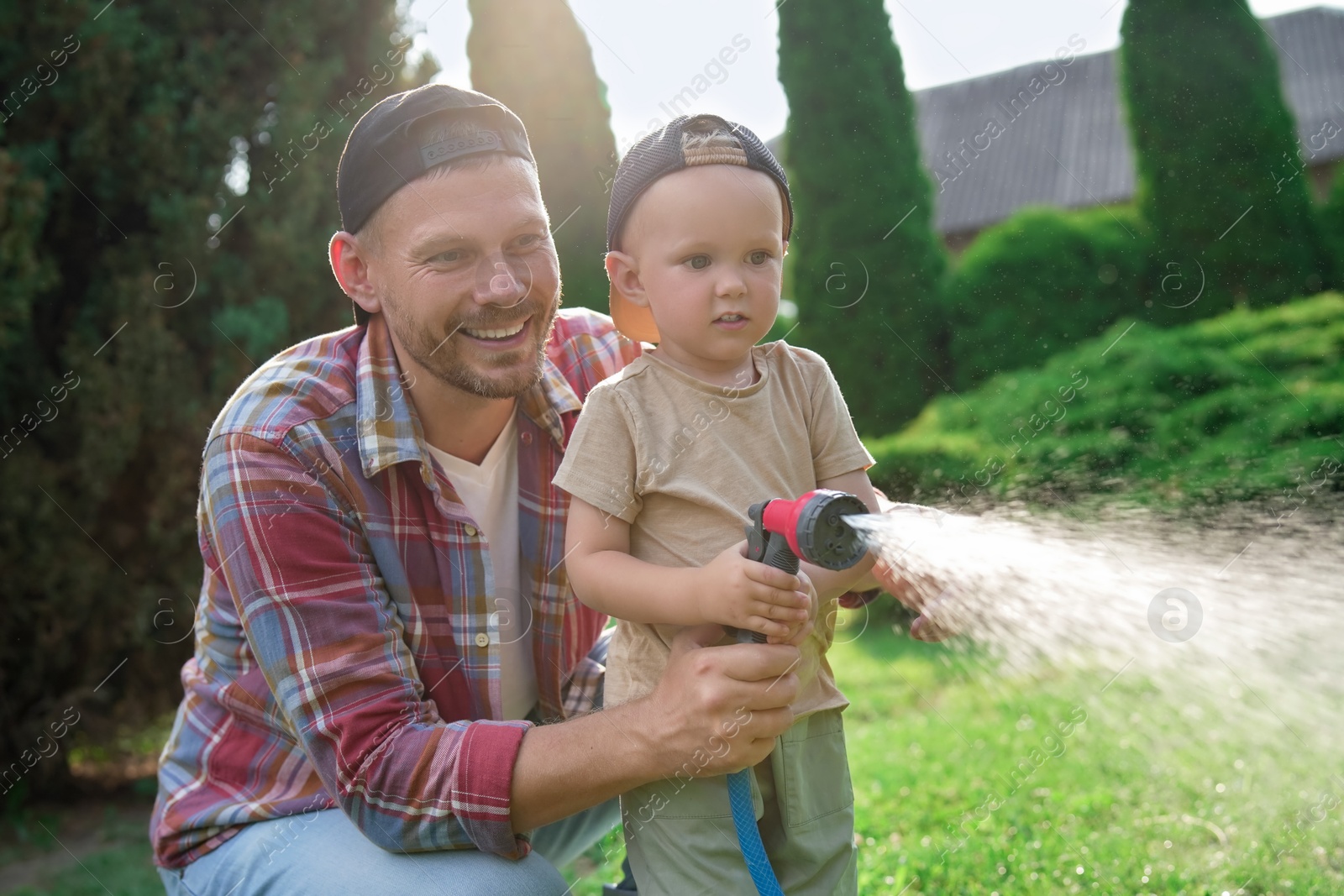 Photo of Father and his son watering lawn with hose in backyard