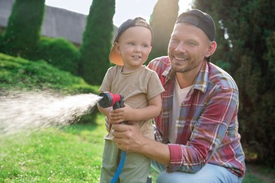 Photo of Father and his son watering lawn with hose in backyard