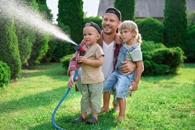 Father and his kids watering lawn with hose in backyard