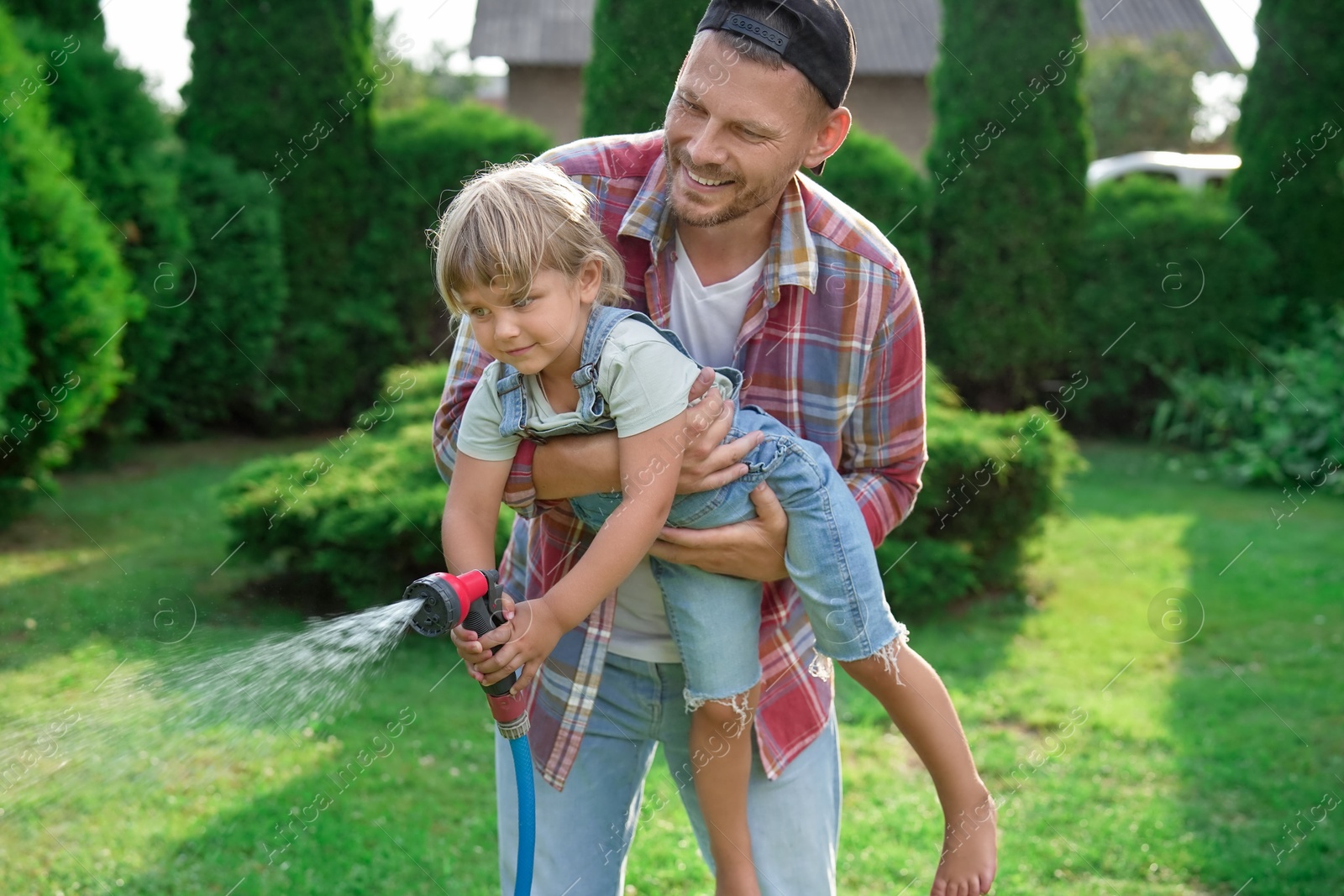 Photo of Father and his daughter watering lawn with hose in backyard