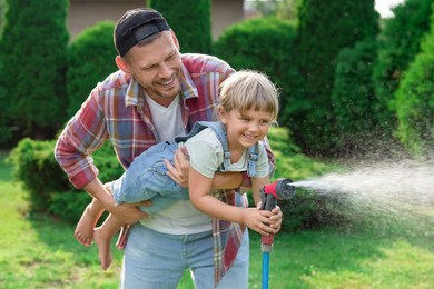 Father and his daughter watering lawn with hose in backyard