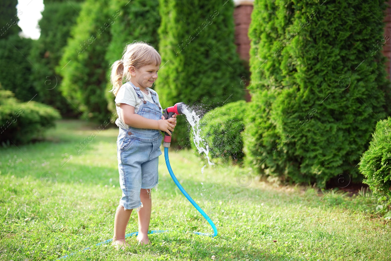 Photo of Little girl watering lawn with hose in backyard, space for text