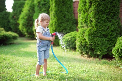 Little girl watering lawn with hose in backyard, space for text