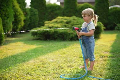 Photo of Little girl watering lawn with hose in backyard