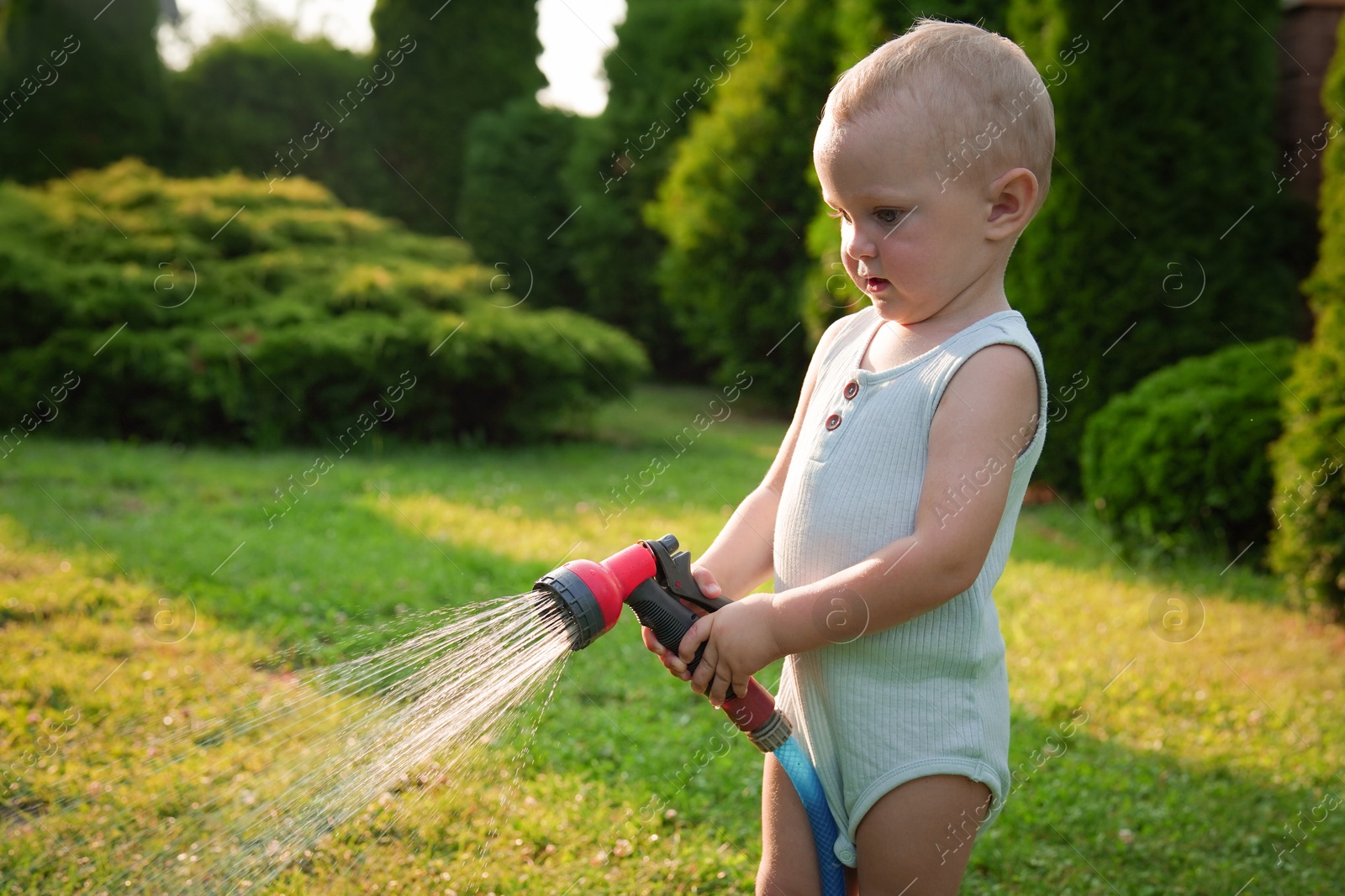 Photo of Little boy watering lawn with hose in backyard