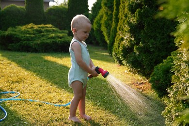 Photo of Little boy watering green grass on lawn in backyard