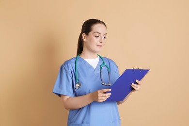 Photo of Portrait of professional nurse with stethoscope and clipboard on dark beige background