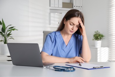 Photo of Tired nurse working at desk in hospital