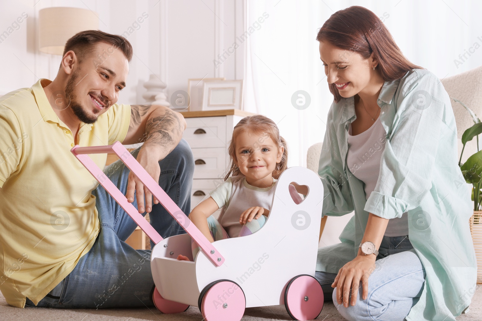 Photo of Happy family. Parents and their cute little daughter in wooden stroller at home