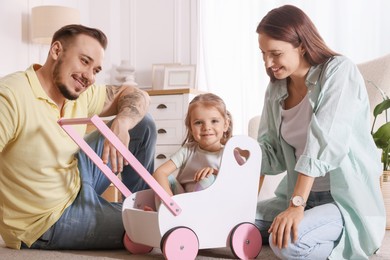 Happy family. Parents and their cute little daughter in wooden stroller at home