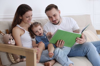 Photo of Happy family. Parents and their cute little daughter reading book at home