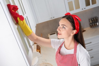 Beautiful young woman cleaning furniture with rag in kitchen