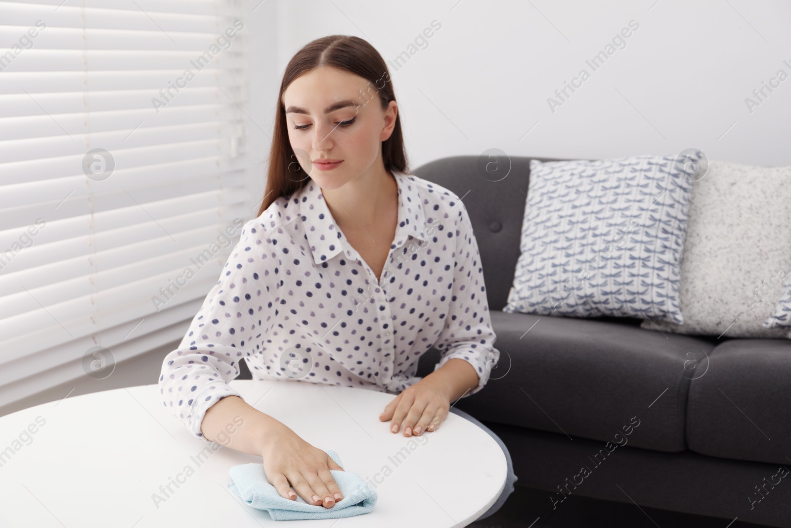 Photo of Beautiful young woman wiping coffee table with rag at home