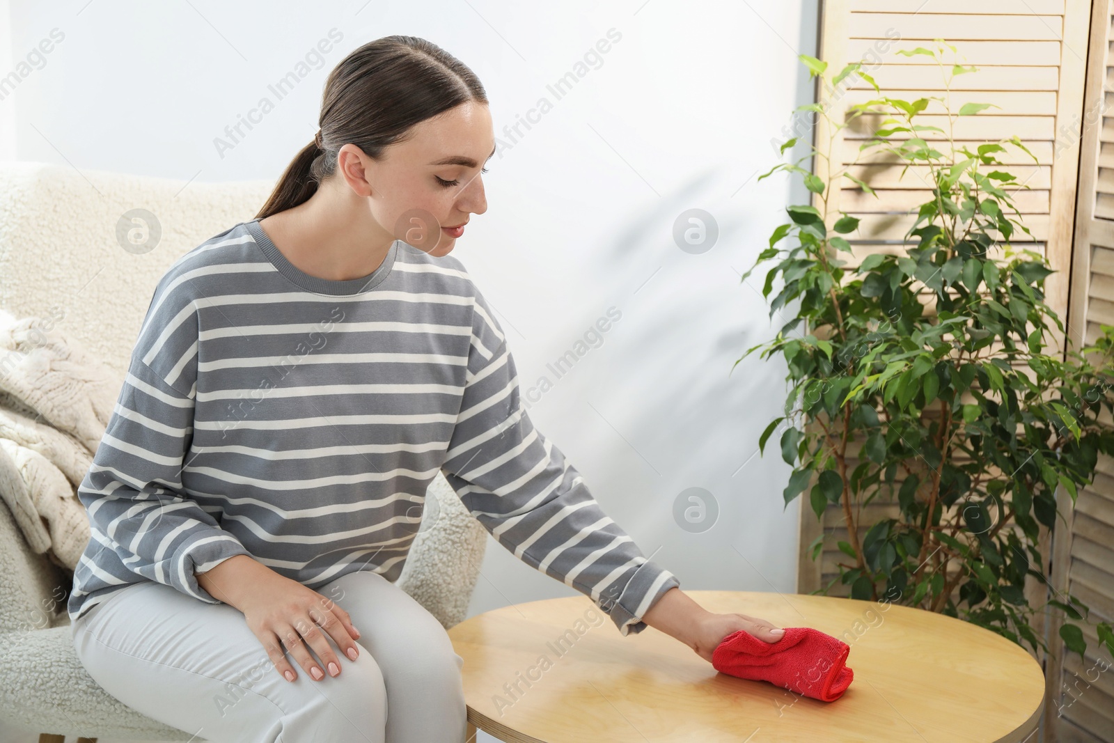 Photo of Beautiful young woman wiping coffee table with rag at home