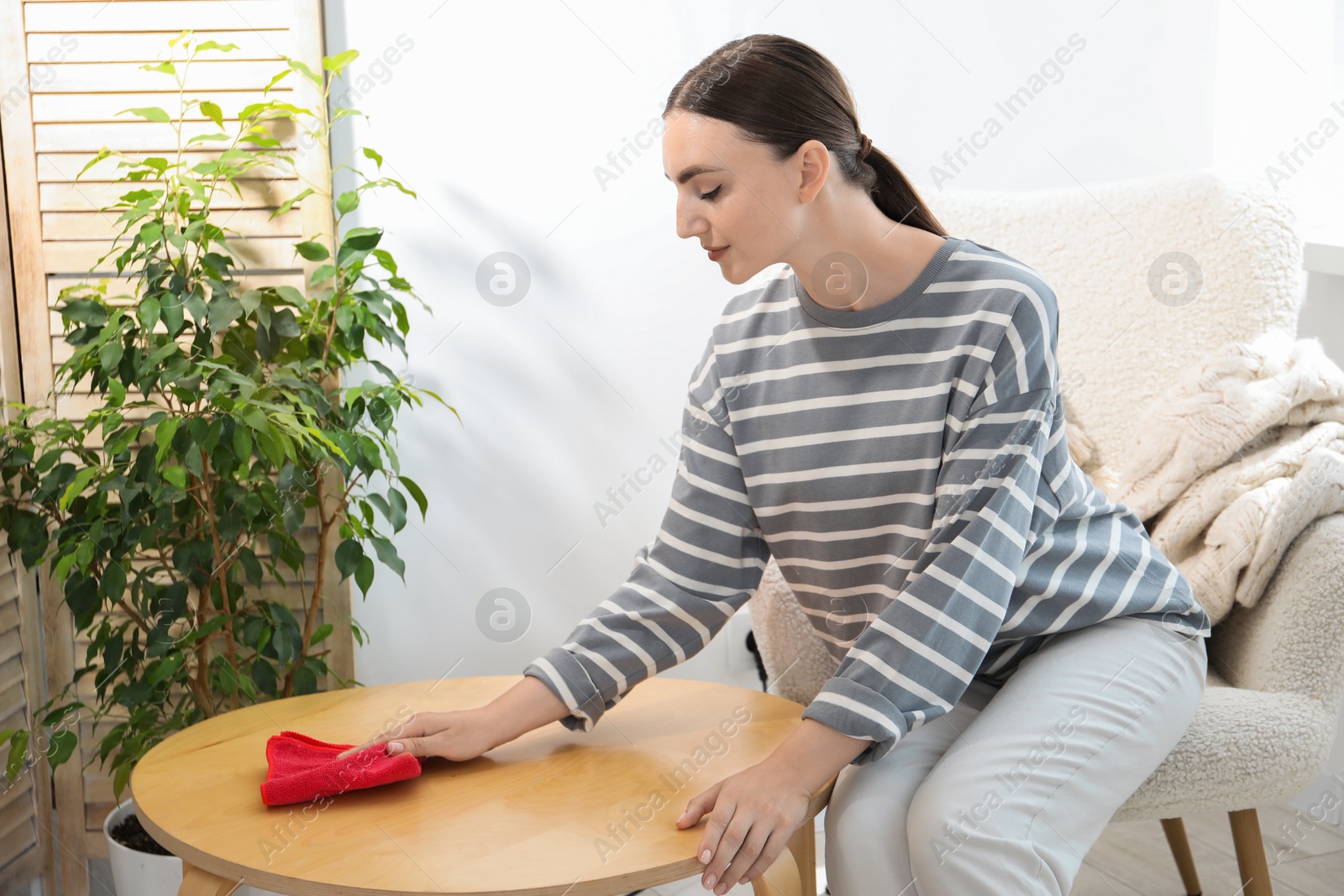 Photo of Beautiful young woman wiping coffee table with rag at home