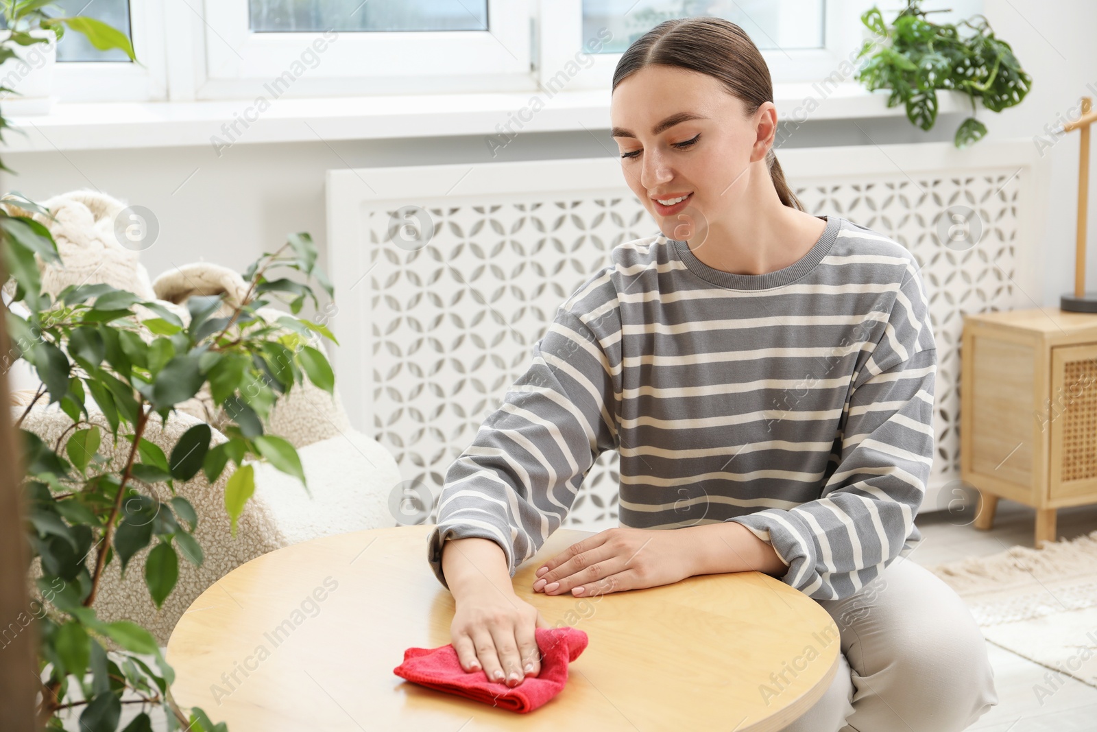 Photo of Beautiful young woman wiping coffee table with rag at home