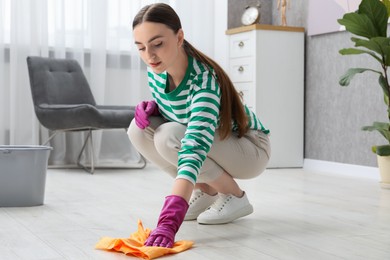 Beautiful young woman cleaning floor with rag at home