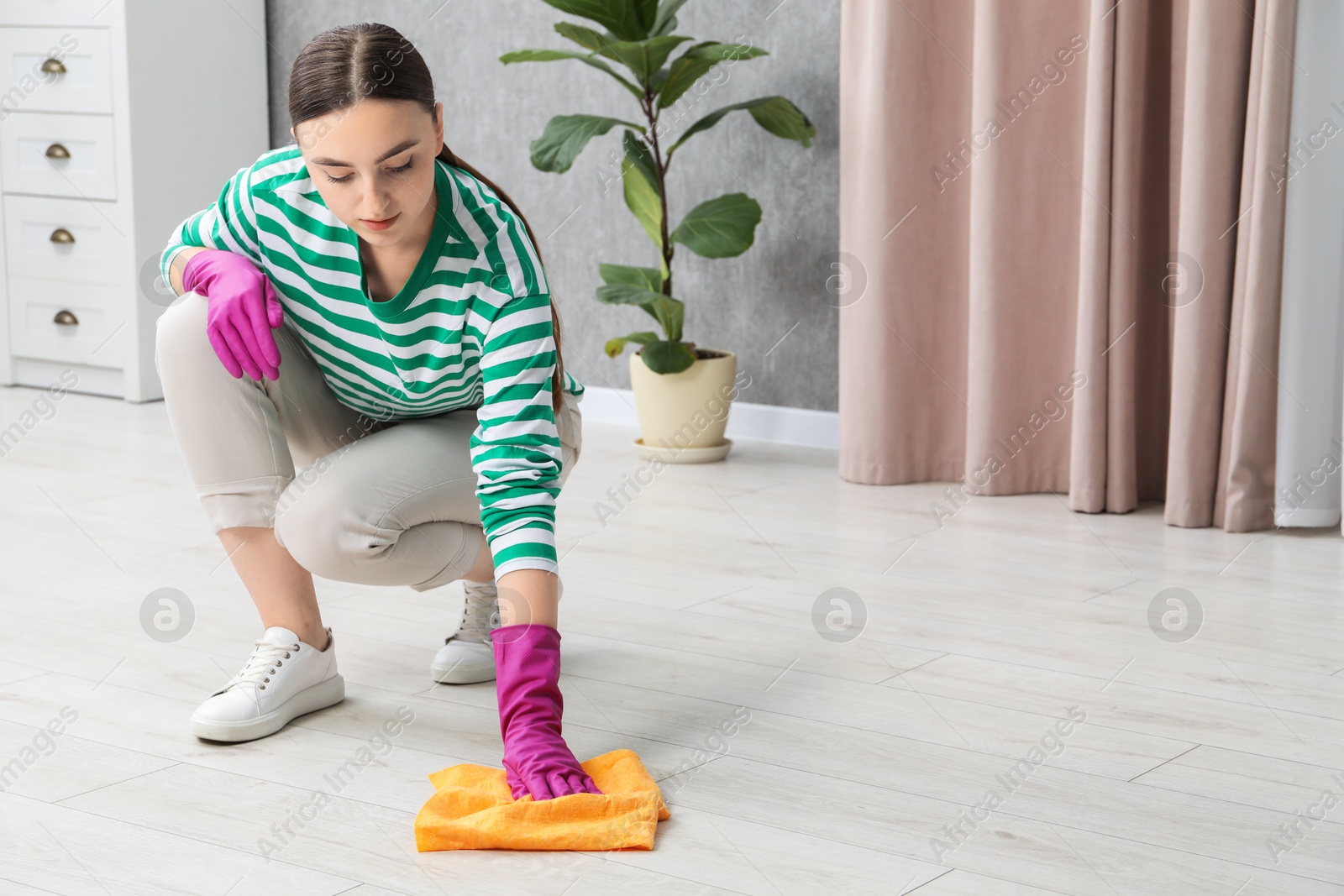 Photo of Beautiful young woman cleaning floor with rag at home, space for text